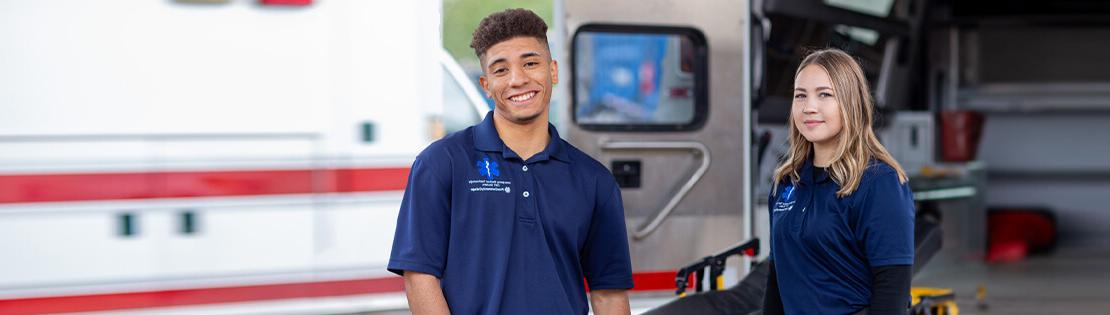Two EMT students smile and pose in the back of an ambulance