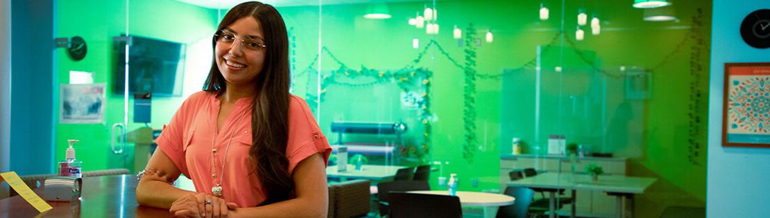 A student worker stands smiling in a student resource center at Pima's Northwest campus