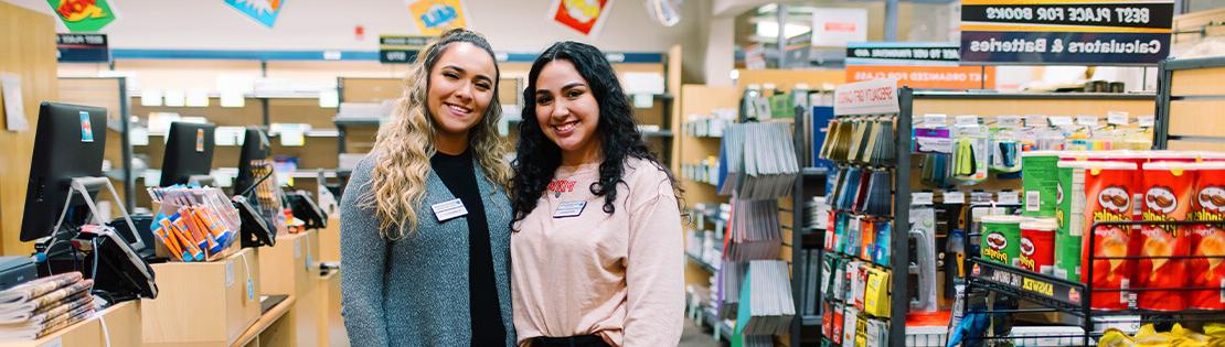 Two Student workers stand smiling in a Pima Bookstore